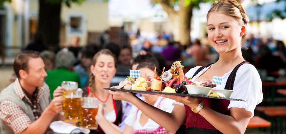 Eine Bedienung in Tracht serviert das Essen in einem Biergarten in München